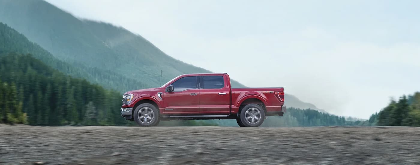 A red 2020 Ford F-150 XLT is shown from the side driving on a dirt road.