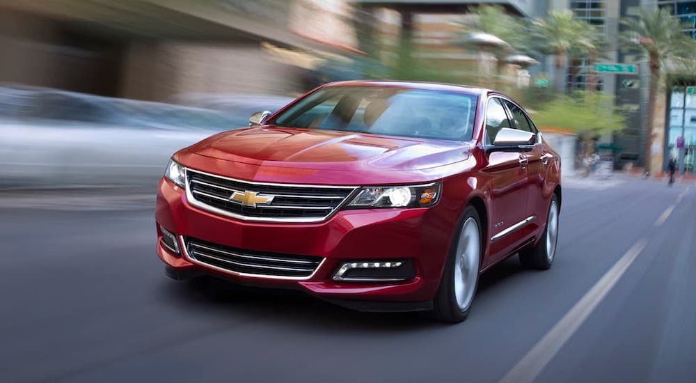 A red 2018 Chevy Impala LTZ speeding down a city street near a used car dealership.
