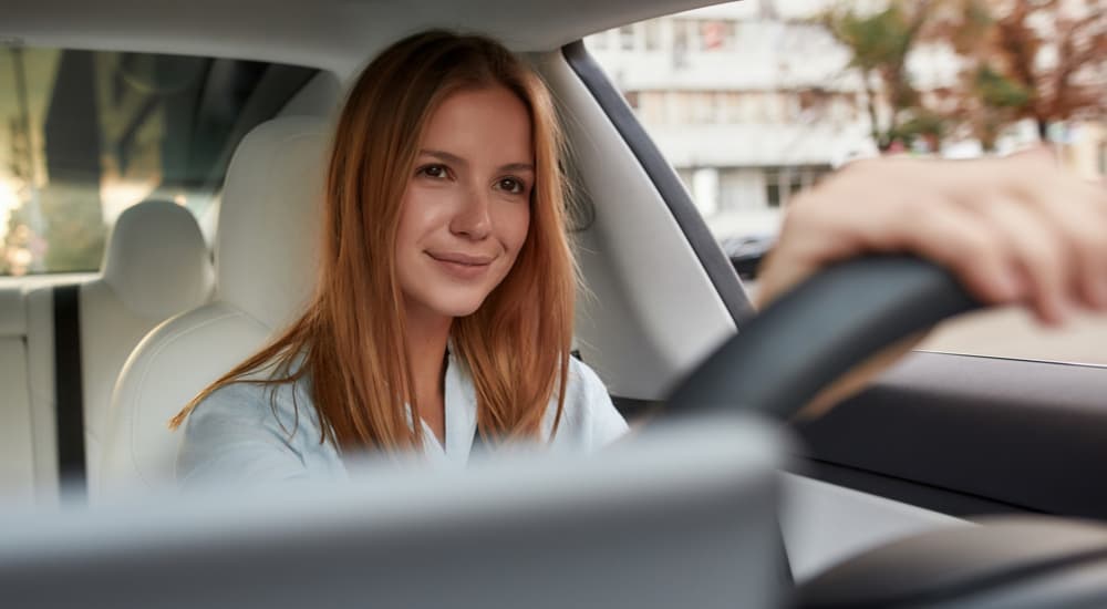 A smiling woman driving to sell her car to a dealer.