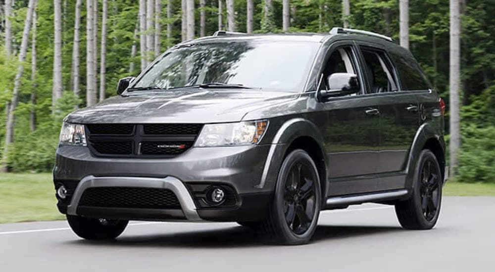 A grey 2020 Dodge Journey parked in an empty lot surrounded by trees.