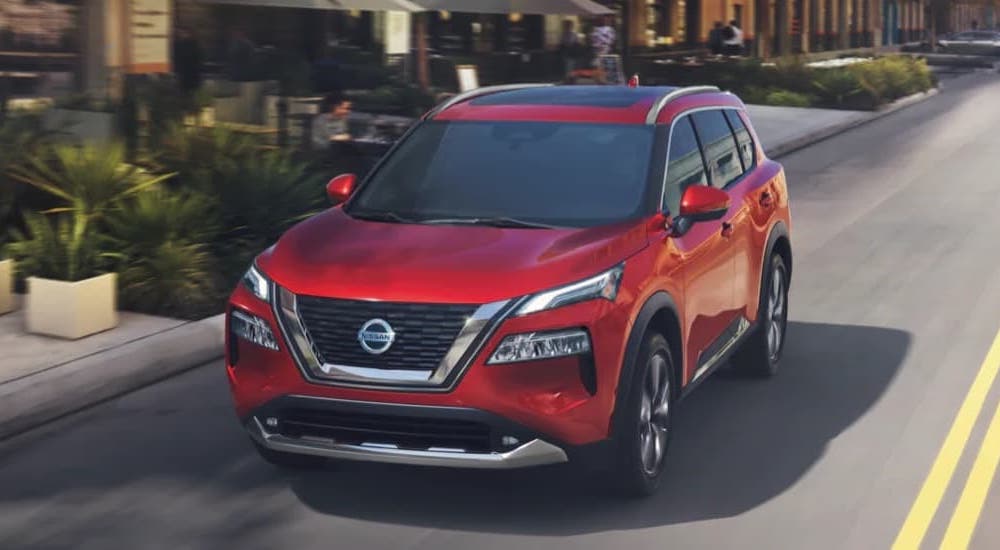 A red 2022 Nissan Rogue is shown driving on a city street after leaving a used Nissan dealer.