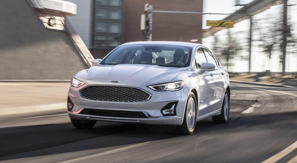 A white 2014 Ford Fusion is shown driving on a winding city road.