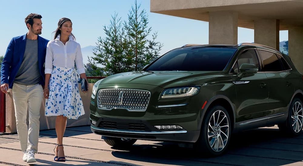 A well-dressed couple walking past a green 2022 Lincoln Nautilus.
