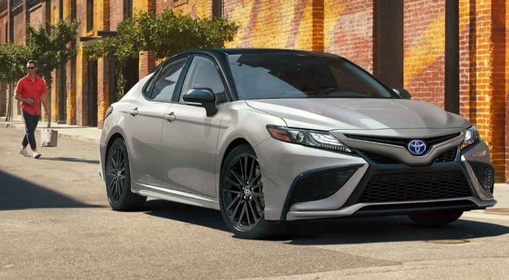 A silver 2022 Toyota Camry XSE Hybrid parked near a brick building after looking at used cars for sale.