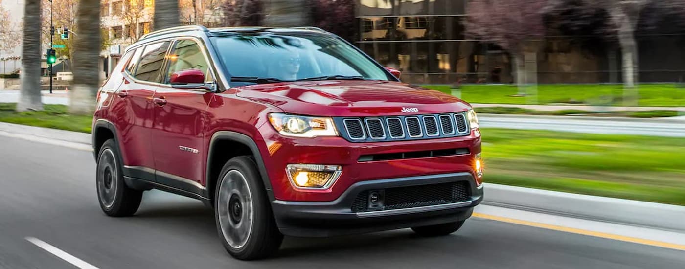 A red 2021 Jeep Compass is shown driving on a city street after leaving a used Jeep dealer.