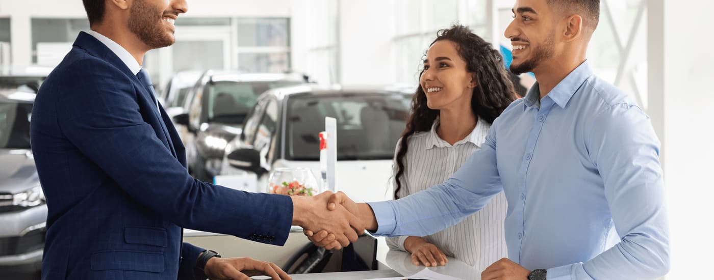 A couple is shown shaking hands with a car salesman after asking about how to sell their car.