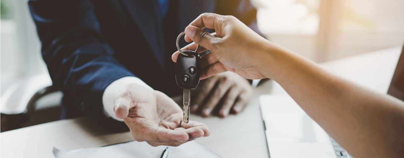 A customer is shown handing a car key to a car salesman.