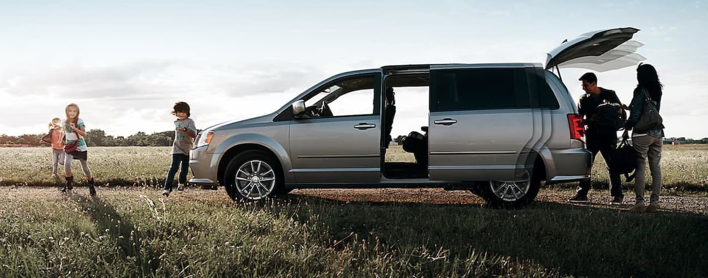 A family is shown getting cargo from the rear of a silver 2020 Dodge Caravan parked near a field.