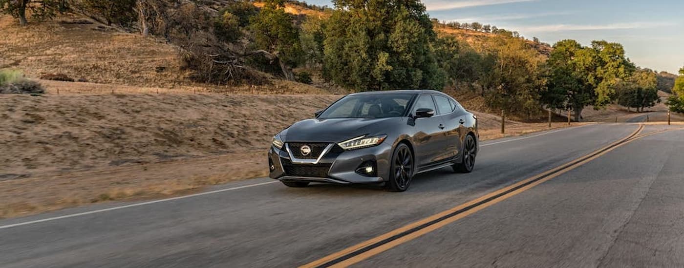 A grey 2020 Nissan Maxima is shown driving on an open road after leaving a used Nissan dealer.