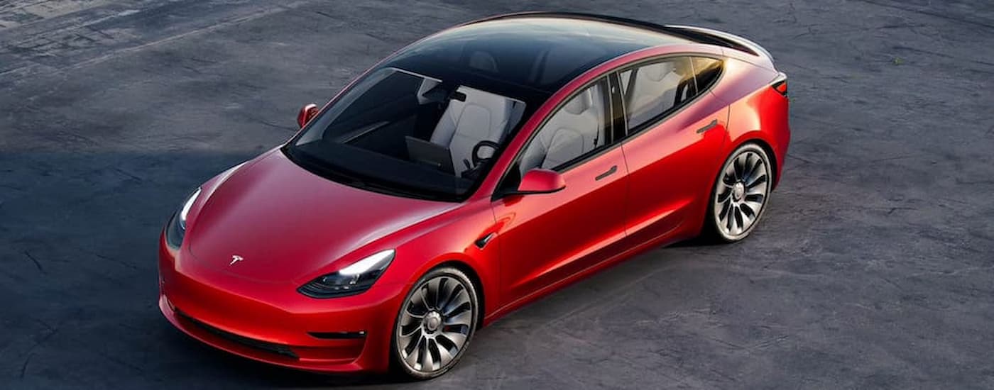 A red Tesla Model 3, a popular electric car for sale, is shown parked on an open lot.