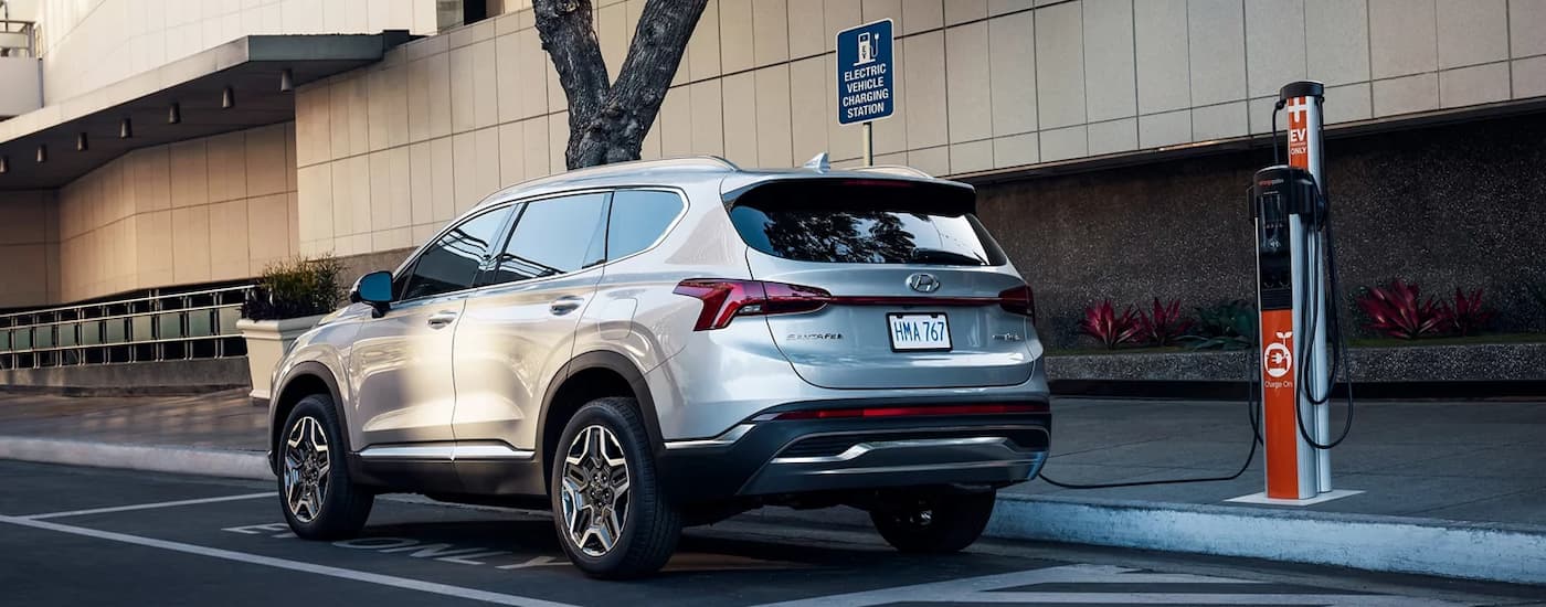 A silver 2022 Hyundai Santa Fe PHEV is shown plugged into an charging station.