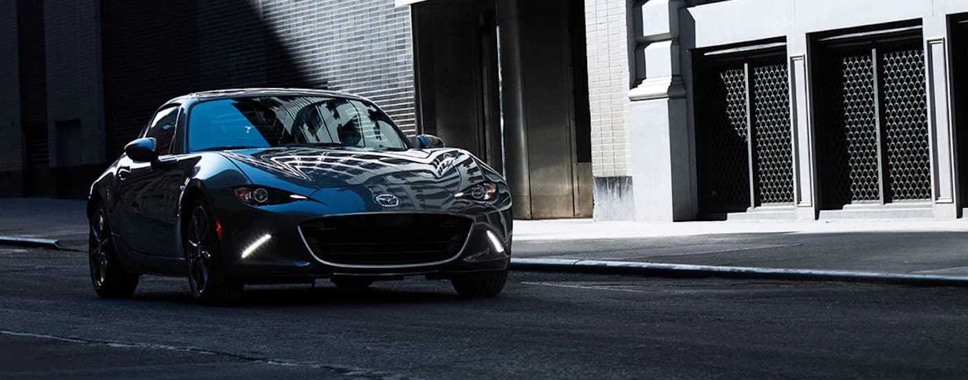 A black 2022 Mazda MX-5 RF is shown parked on the side of a city street.