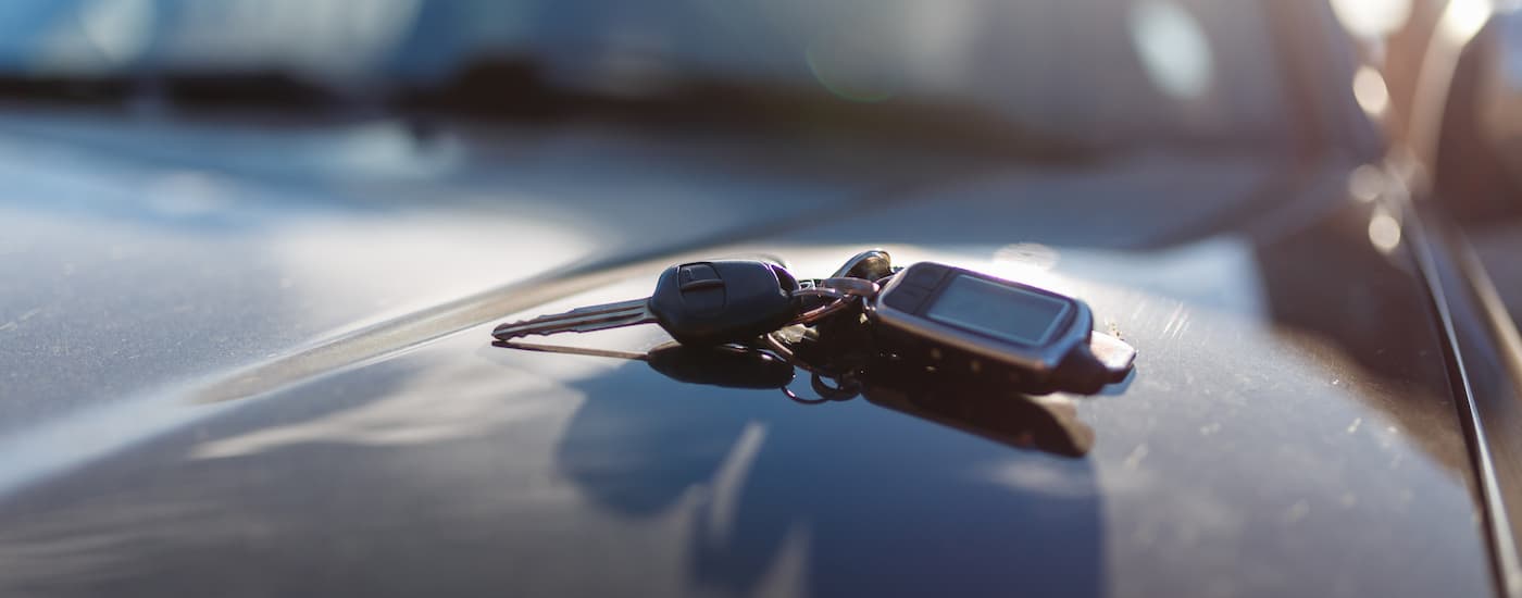 A set of car keys are shown on the roof of a certified pre-owned car.