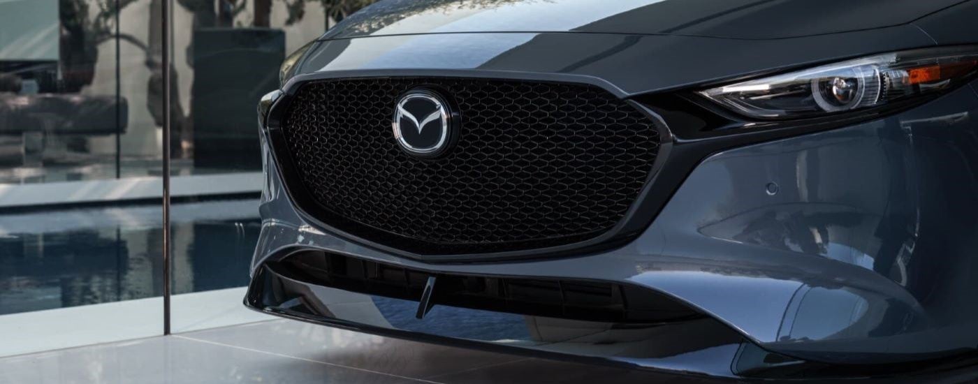 A close up shows the grille on a grey 2021 Mazda3 at a used car dealership.