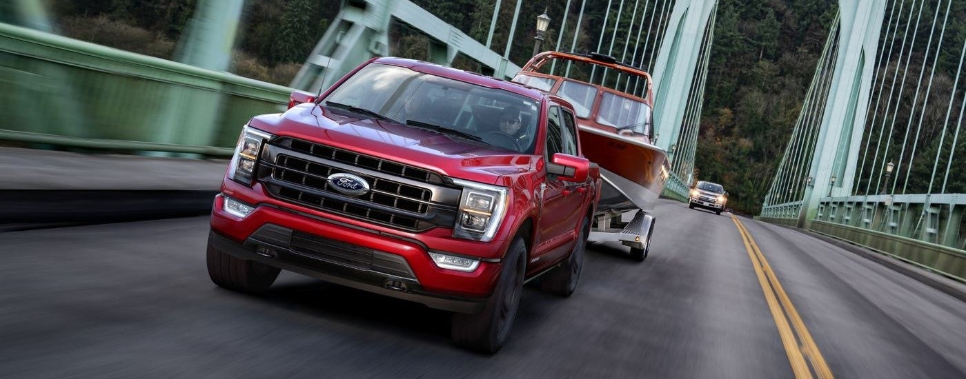 A red 2021 Ford F-150 is shown towing a boat over a bridge after leaving a used Ford dealer.